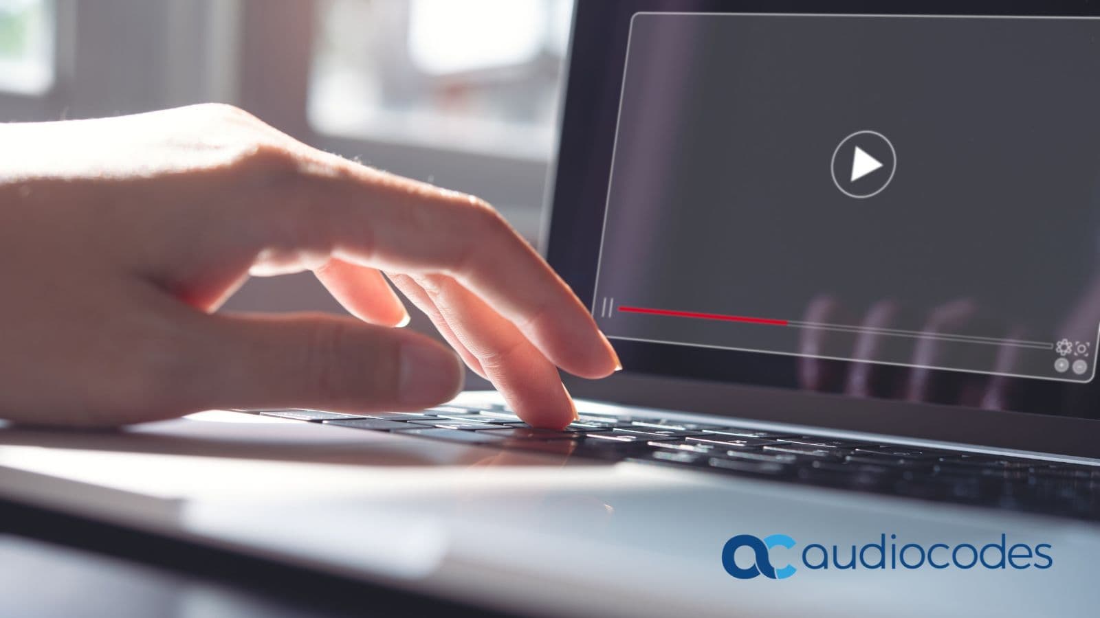 Close-up of a hand at a laptop keyboard about to play a video interview, branded with the AudioCodes logo
