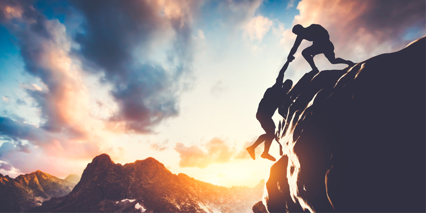 Man giving hand, helping his colleague to climb the mountain