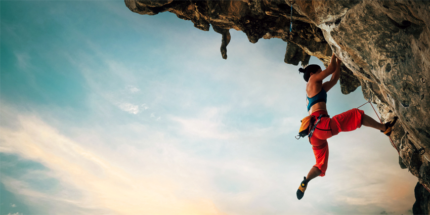 Athletic Woman climbing on overhanging cliff rock with sunset sky background.