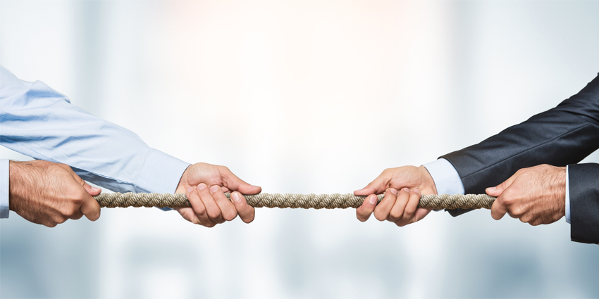 Tug of war, two businessman pulling a rope in opposite directions over defocused background with copy space