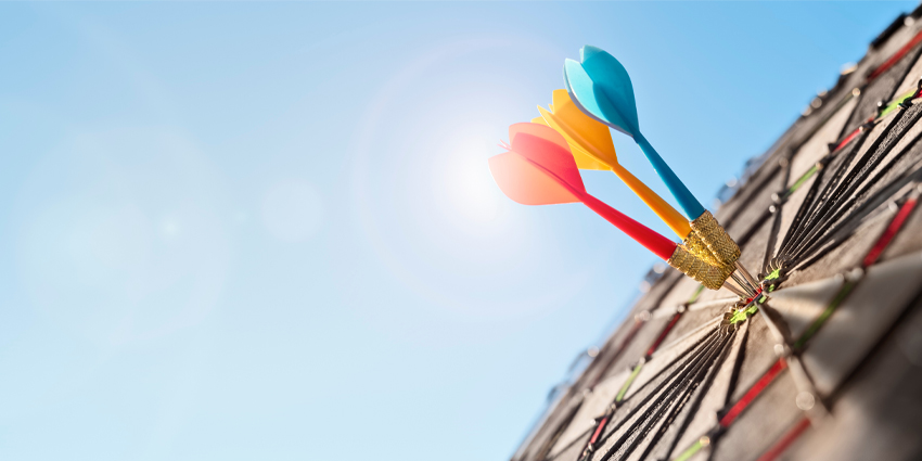 Dart in bullseye of dartboard with blue sky background hitting target, goal and success