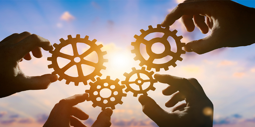 Four hands of businessmen collect gear from the gears of the details of puzzles. against the backdrop of dramatic sunlight.