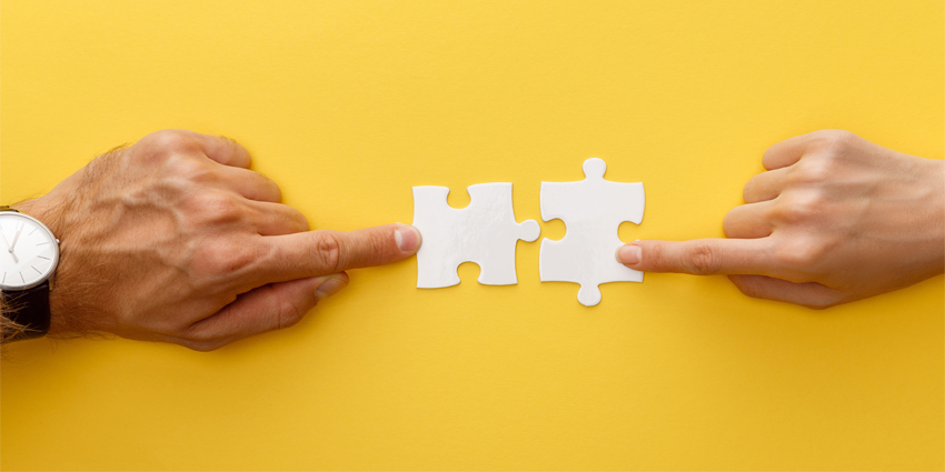 cropped view of woman and man matching pieces of white jigsaw puzzle on yellow background