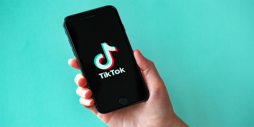 Studio shot of hand holding Apple iPhone 8 with TikTok logotype on a screen. Isolated on a vibrant cyan paper background.