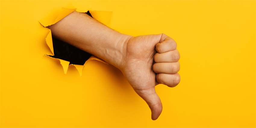 Hand shows a thumb down through a hole of yellow paper wall